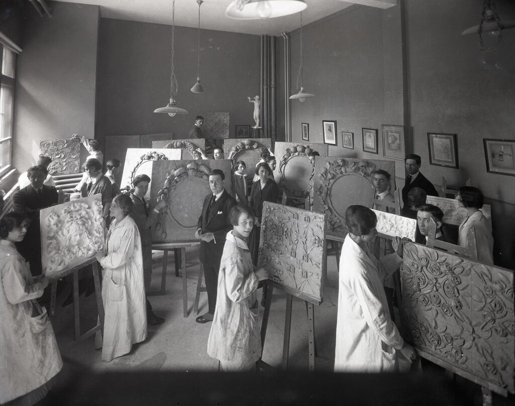 Des hommes et des femmes debout dans une salle de classe, travaillant avec du plâtre sur des toiles posées sur des chevalets