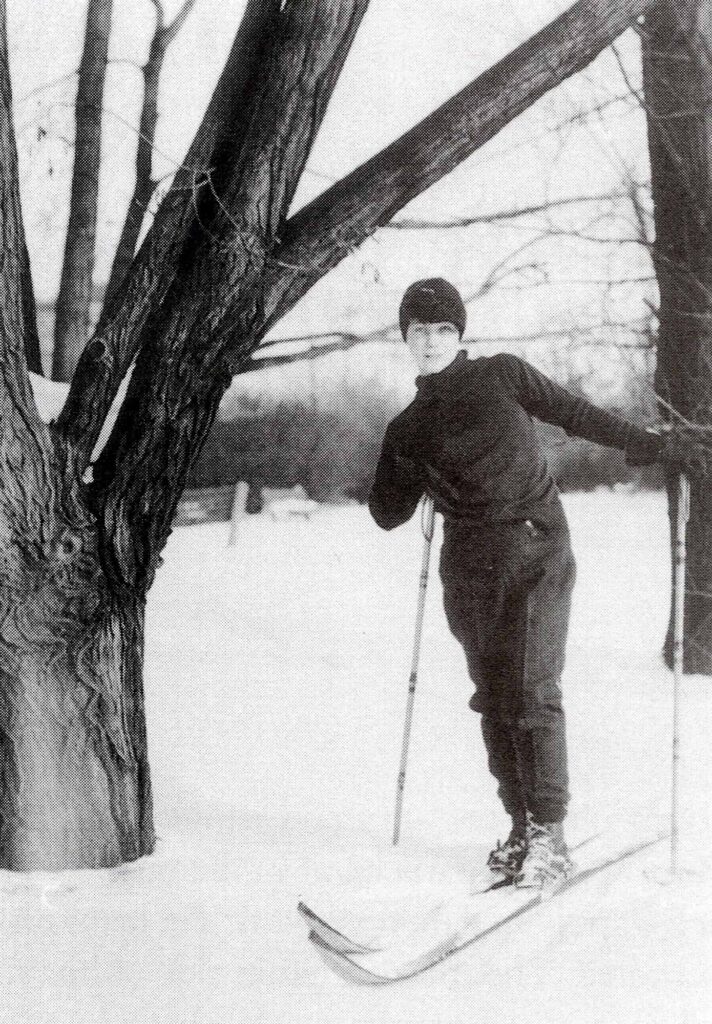 Photographie en noir et blanc représentant des femmes à skis près d'un arbre dans la neige.