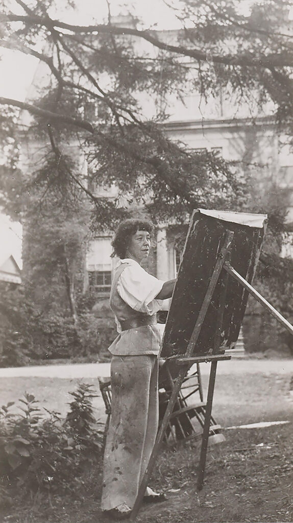 Photographie en noir et blanc d'une femme peignant en plein air sur une toile posée sur un chevalet