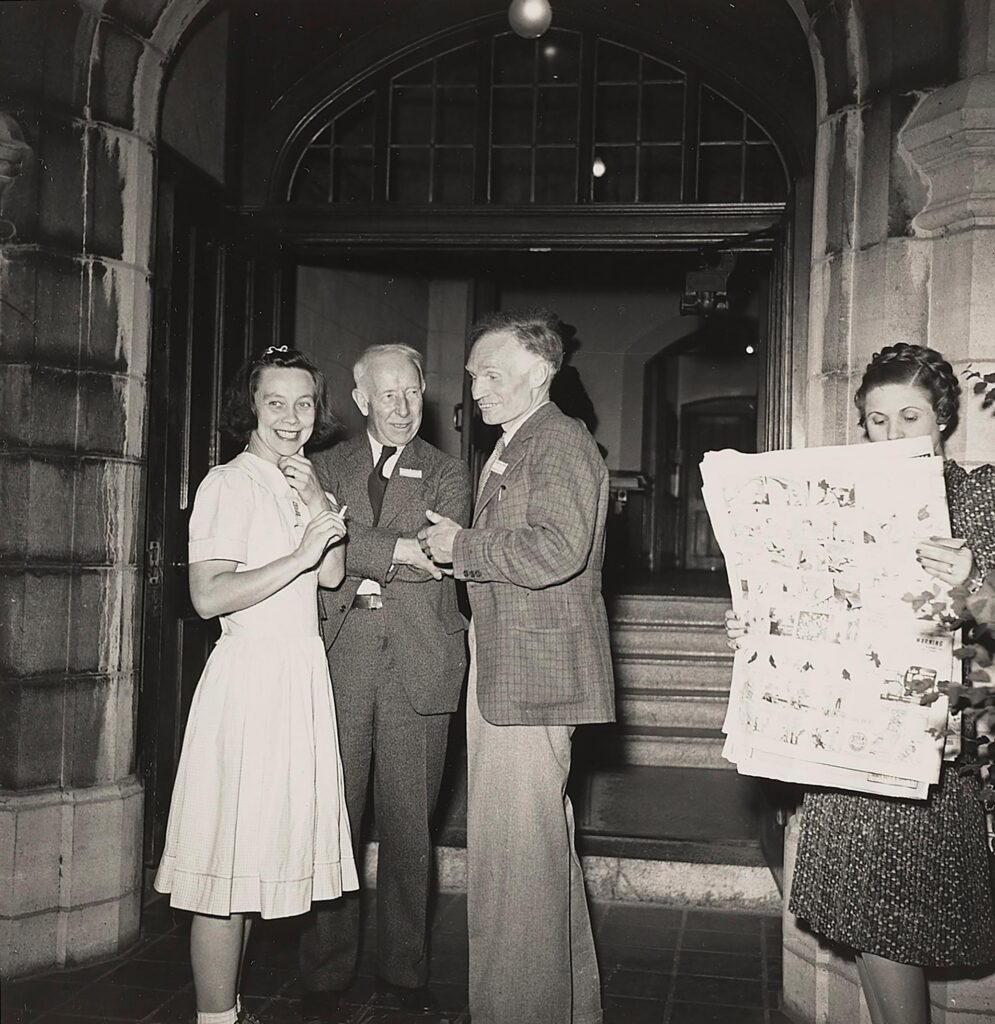Photographie en noir et blanc représentant une femme, deux hommes et une autre femme en train de lire un journal.