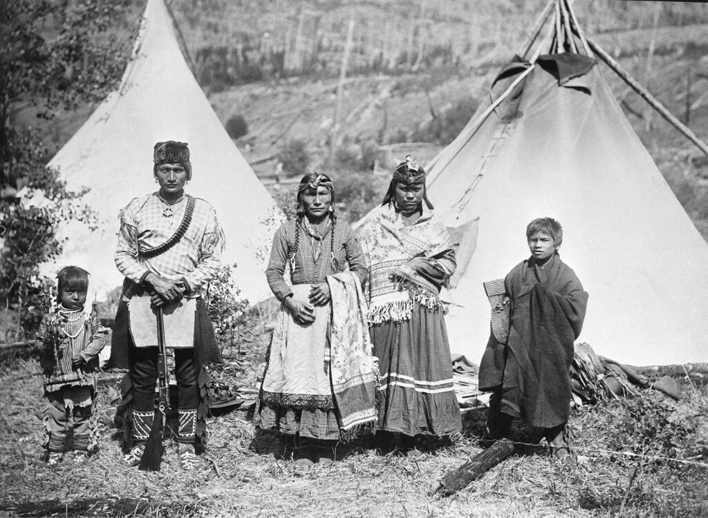 Black and white photograph of five people in traditional clothing in front of two white tents.