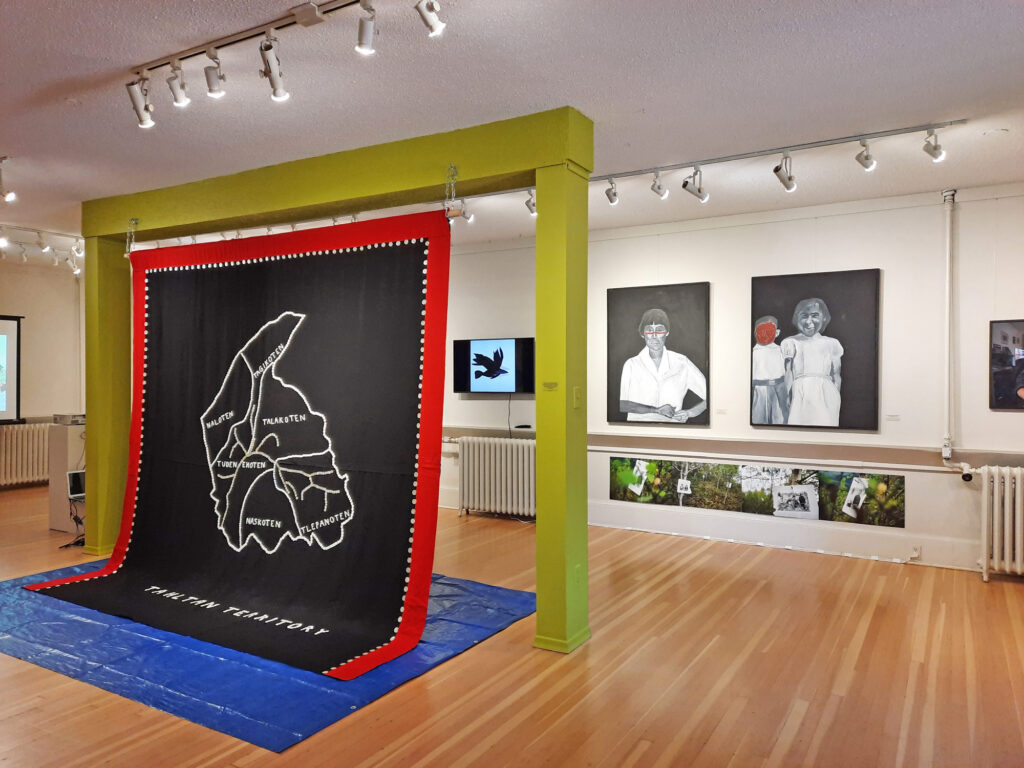 A gallery scene featuring a black blanket decorated with a white map.