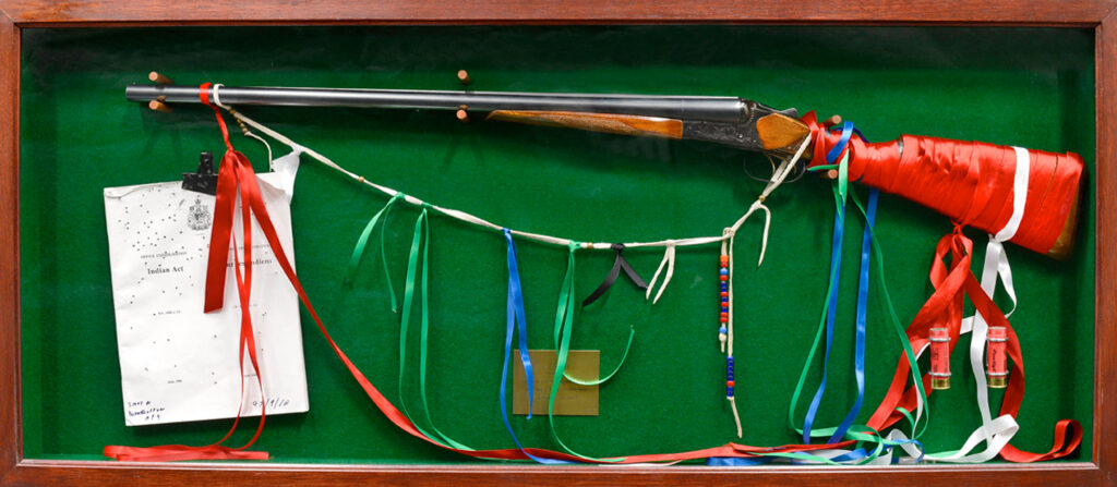A shadow-box of a document, shotgun, ribbons and other elements against green baize.