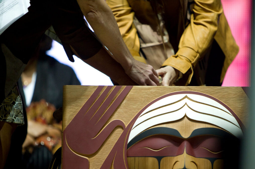 People gather around a bentwood box in a ceremony.
