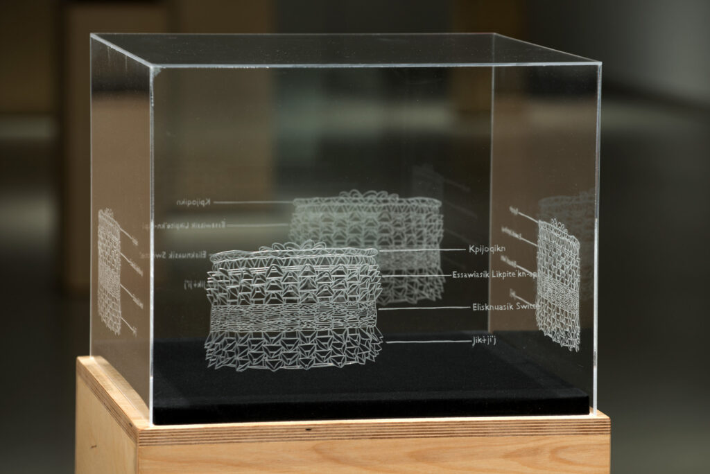 A plexiglass box with engraved sides in a gallery.