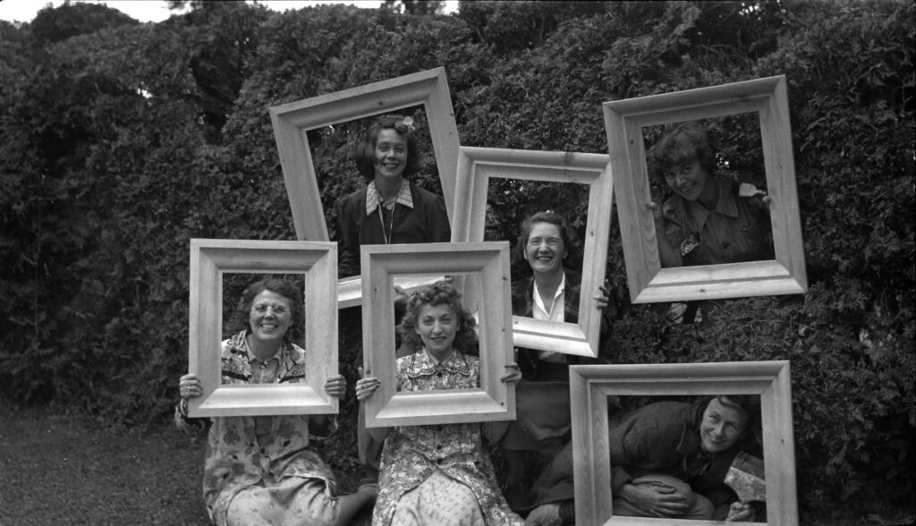Photographie en noir et blanc d'un groupe de femmes posant en tenant des cadres vides autour de leur visage.