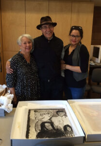 Photograph of three family members posing before an illustrated family portrait.