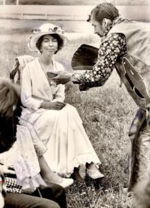 black and white photo of a woman sitting a chair outside with a man leaning down towards her